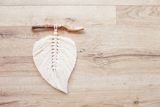 istock Macrame leaf  in natural color and thread windings lying on a wooden table. Cotton rope decor macrame to make your room more cozy and unique. Woman hobby. Handmade wall hanging decor. Copy space 1359473295