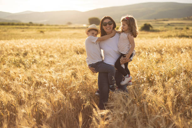 istock Mother carrying her two kids while standing in nature on sunny day 1359473944