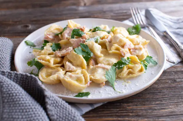 Traditional pasta dish from italy. Tortellini alla panna cooked with ham, parmesan cheese, herbs in a delicious cream sauce. Served isolated on wooden table background