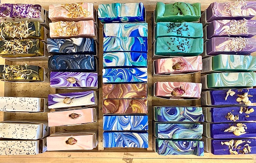 Horizontal flat lay of handmade organic herbal soaps with flowers herbs essential oils dried fruit with swirls and vibrant variety of colors sliced in display wood box