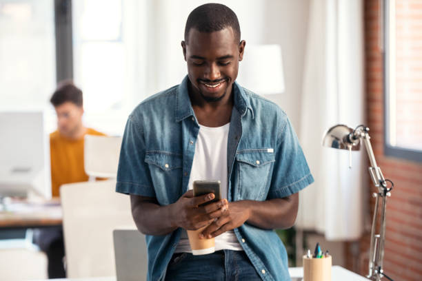 istock Happy businessman using smartphone while drinking a cup of coffee sitting on a desk in a coworking space. 1359483009