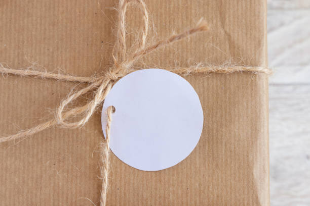 istock Kraft paper wrapped present with round blank gift tag top view, Mockup 1359487311