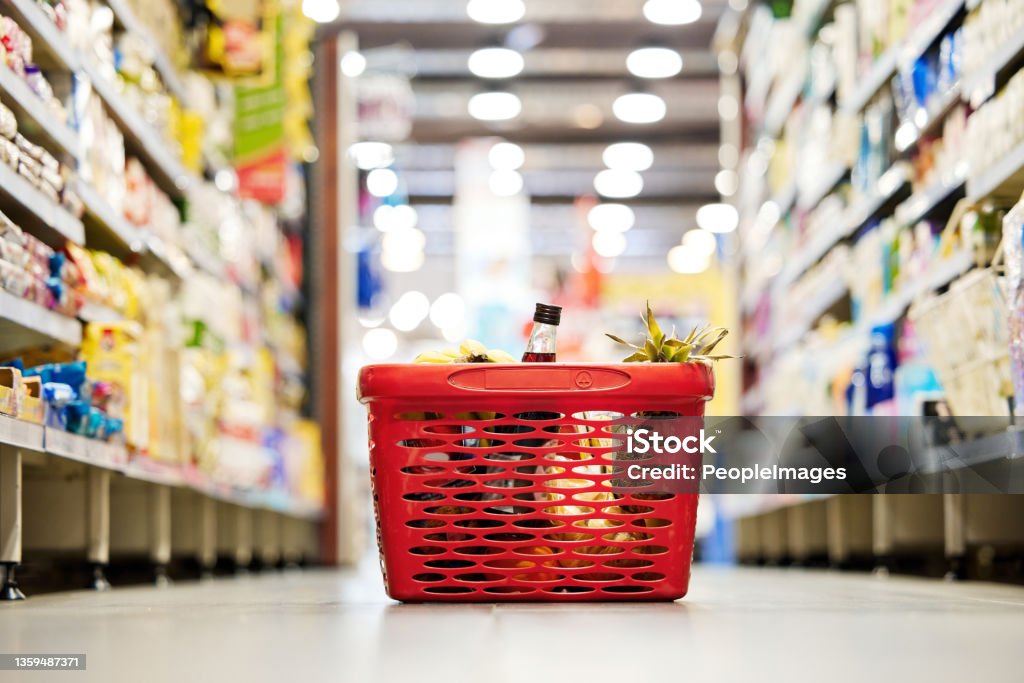 Shot of a shopping basket on the floor of a grocery store The aisle of goodnes Supermarket Stock Photo