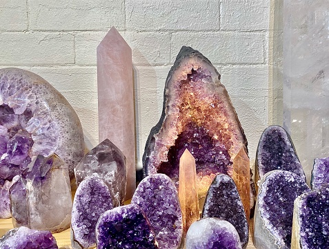 Horizontal close up of a group of large purple amethyst crystal geode cave clusters sparkling together on display against white wall