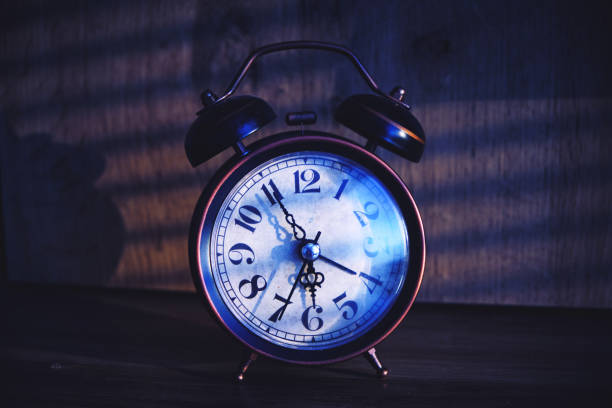 istock Retro alarm clock early morning on table rays sunlight through blinds in bedroom. 1359488203