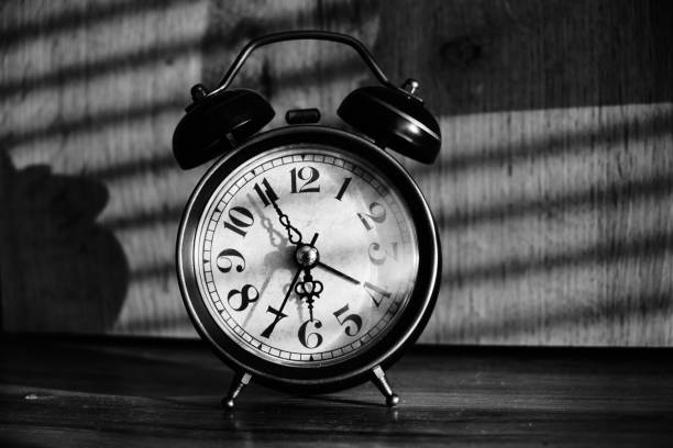 istock Retro alarm clock early morning on table rays sunlight through blinds in bedroom. 1359488212