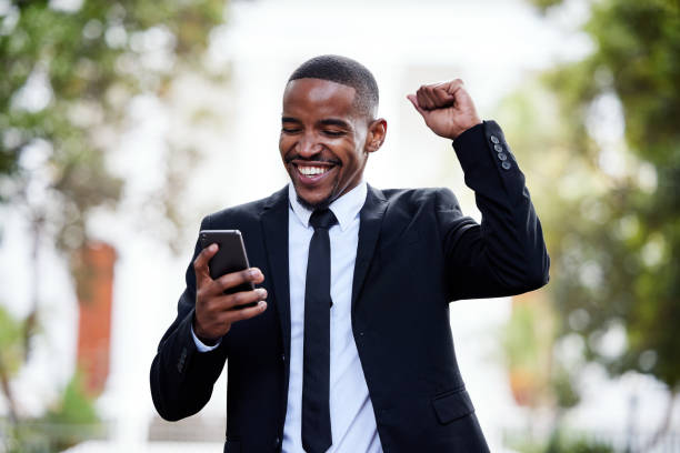scatto di un giovane uomo d'affari che applaude mentre usa un telefono in città - excitement business person ecstatic passion foto e immagini stock