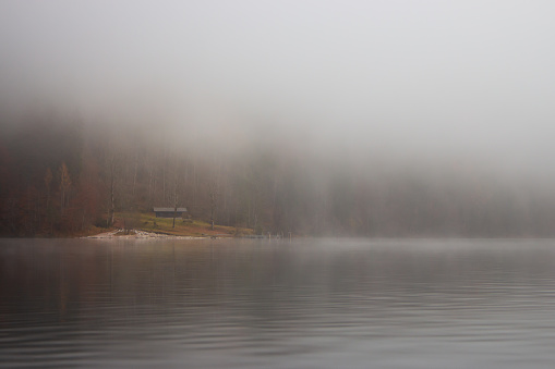 Fog on the lake Kenigsee, Germany. Old wooden house on the bank in fog. Mist on riverbank. German landscape. Autumn scenery in Europe, national Berchtesgaden park.