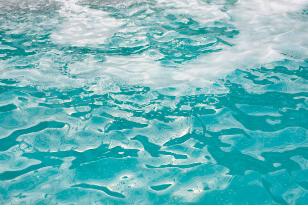 Textured water surface with waves and foam, clear blue pool water Textured water surface with fine waves and foam, clear blue pool water spume stock pictures, royalty-free photos & images