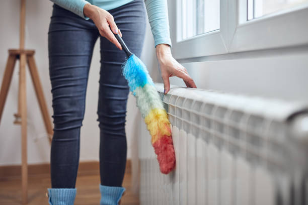 mujer con un palo de polvo limpiando el radiador de gas de calefacción central en casa. - dust dusting cleaning broom fotografías e imágenes de stock