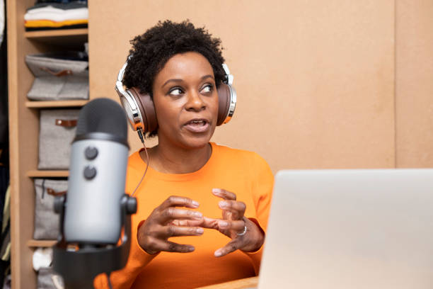 donna espressiva che registra un podcast a casa in camera da letto - con cuffie, microfono e un laptop - cool business looking at camera posing foto e immagini stock