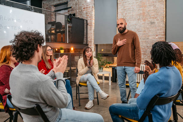 Man talking to the other members of the therapy group Sad young man sharing his experience and problems with depression to a members of a support group. alcoholics anonymous photos stock pictures, royalty-free photos & images