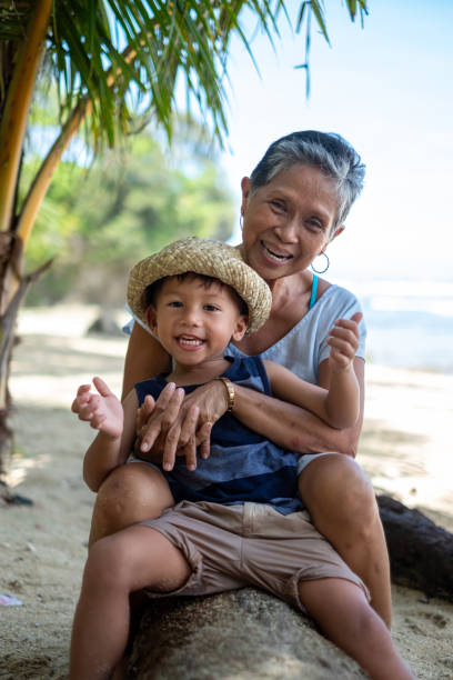 Grandmother bonds with grandson on the beach Grandson sitting with grandmother on the beach filipino family stock pictures, royalty-free photos & images