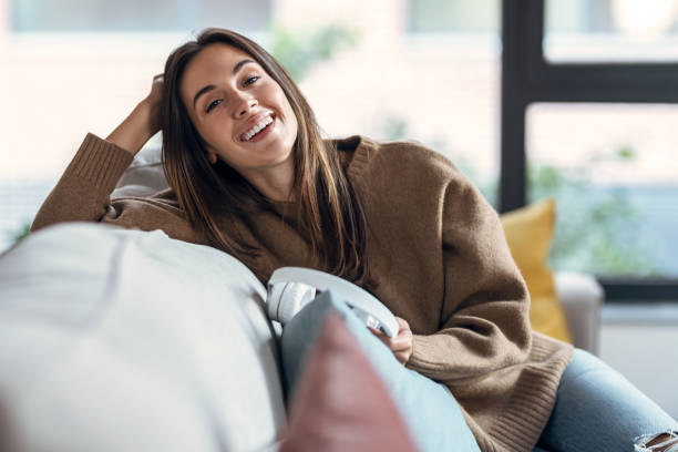 istock Beautiful woman relaxing while looking at camera on sofa at home. 1359500172