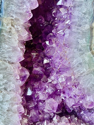 Vertical close up still of inside the cave of large purple amethyst crystal geode cluster sparkling with rock edges