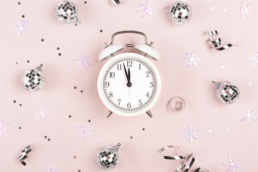 White retro clock shows almost 12. Countdown to midnight. Christmas and New Year concept. Trendy flatlay style.