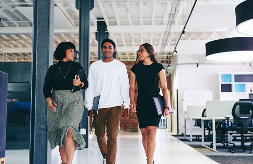 Businesspeople on the move. Group of three confident businesspeople talking to each other while walking together in a modern office. Colleagues working together in a creative workplace.