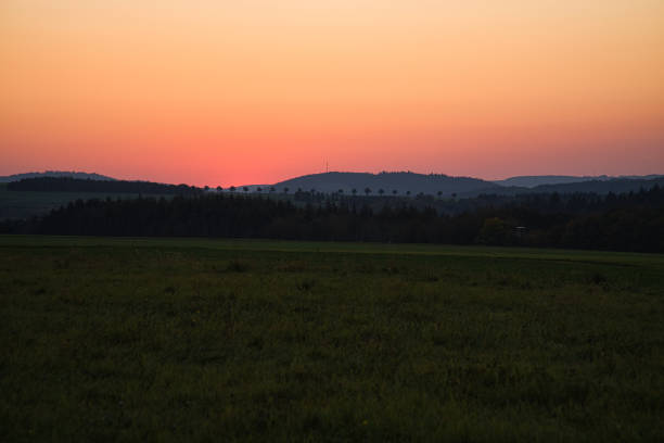 romantic sunset behind a hill in front of a meadow. Tuscan view with the row of trees in the background