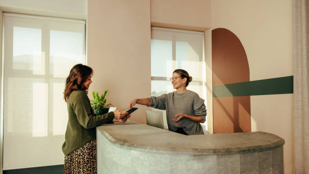 carefree receptionist assisting a woman with signing in to an office - recepção imagens e fotografias de stock