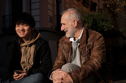 Asian teenage boy, adopted son, and Caucasian adult man, adopted single father, chatting on street. Madrid. Spain