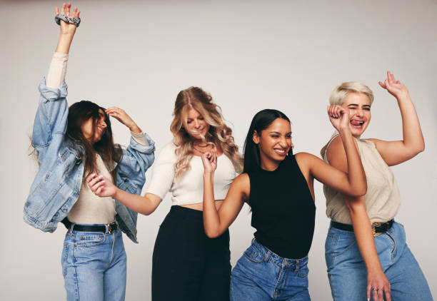 Group of female friends dancing in a studio Group of female friends dancing cheerfully in a studio. Four happy women celebrating and having fun together. Diverse group of women standing against a grey background. body positive stock pictures, royalty-free photos & images