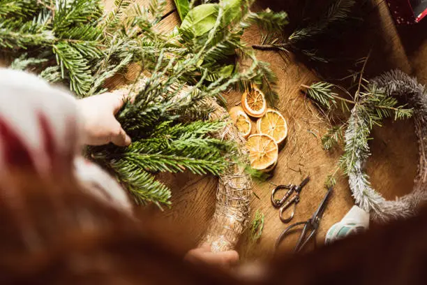 Female making a Christmas wreath in a DIY - Do It Yourself - work at home on a wooden table top with vintage scissors and tools.