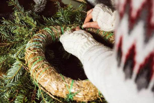 Female making a Christmas wreath in a DIY - Do It Yourself - work at home on a wooden table top with vintage scissors and tools.