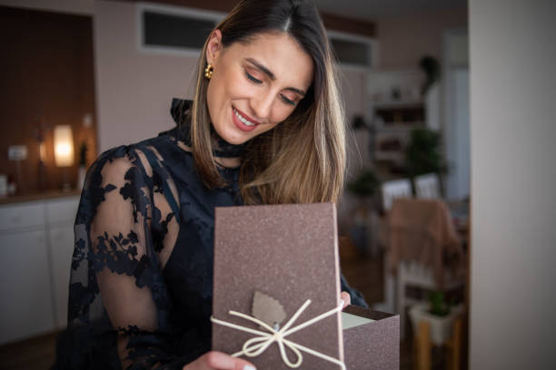 istock A happy woman stands by the window and opens a gift box 1359512515