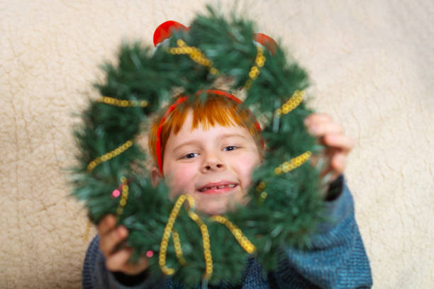 A young boy smiles and holds a Christmas wreath.
