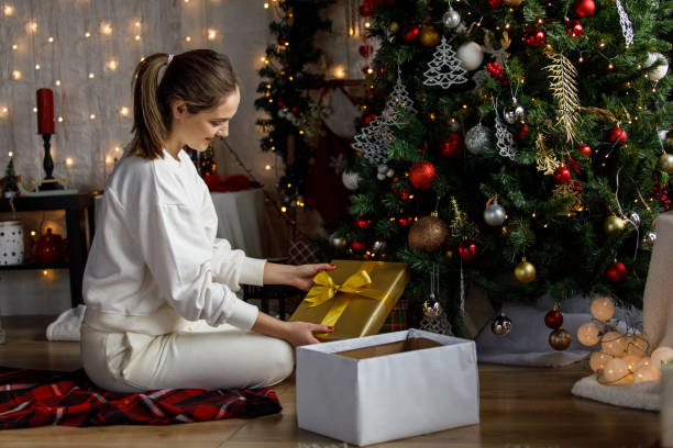 istock Young woman putting a gold colored gift box under the Christmas tree 1359516255