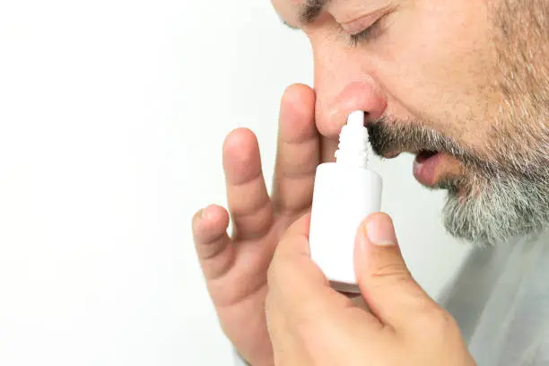 Bearded senior man applying spray for runny nose. Treatment of colds and flu concept