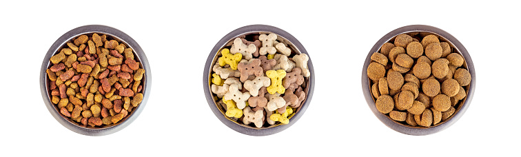 Top view of brown biscuit bones and crunchy organic kibble pieces for dog feed in a metal bowl set isolated on white background. Healthy dry pet food.
