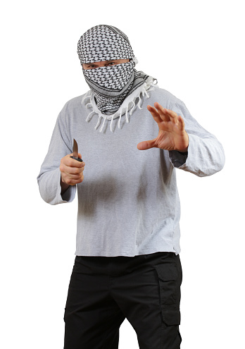 La cara del hombre está enmascarada con la bufanda tradicional de keffiyeh. Sostiene un cuchillo y se prepara para atacar photo