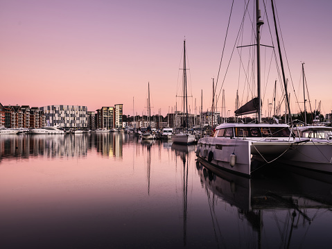 Ipswich, Suffolk, England - December 16 2021: Ipswich Marina waterfront pink sunset with cloudless sky and striking reflections of the adjacent buildings in the water.