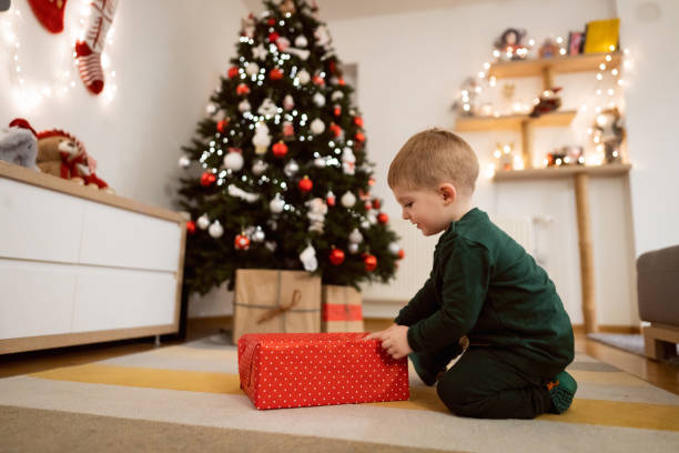 istock Toddler boy near Christmas tree unwrapping his Christmas present 1359521537