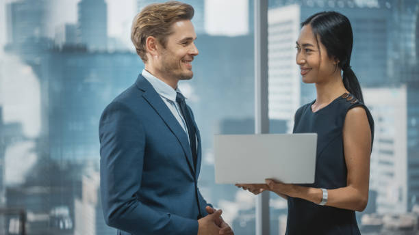 istock Portrait of Successful Corporate CEO and Finance Manager Talking, Using Laptop Computer while Standing in City Office. Stock Market Investors Negotiate e-Commerce Business Purchase. 1359523962
