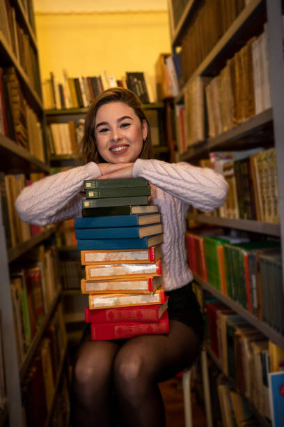 istock beautiful cute happy lady enthusiastically reads one book after another in a modern library. 1359524340