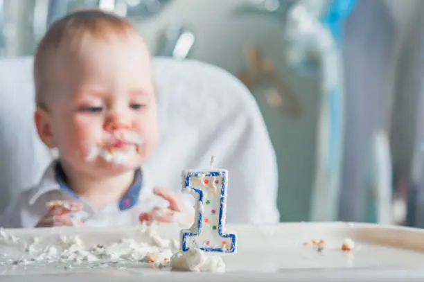Cute toddler boy for first year of birth eating birthday cupcake with 1 candle close-up and copy space.