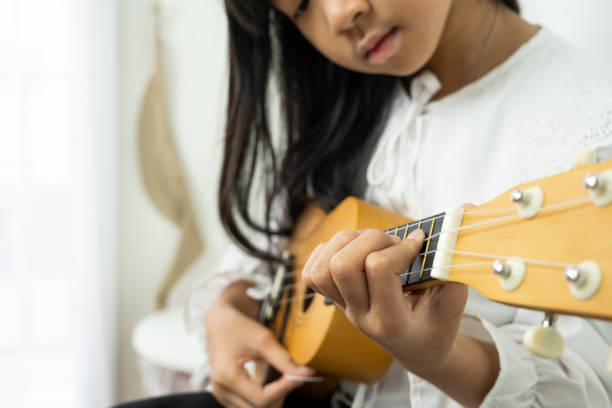 Asian child girl is playing a wooden ukulele Asian child girl is playing a wooden ukulele ukulele stock pictures, royalty-free photos & images