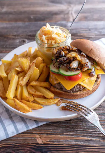 Fresh and homemade cooked fast food meal with a delicious cheeseburger, with fries and coleslaw. Served isolated on wooden table. Vertical image