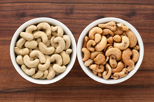 Top view of two bowls side by side with raw and roasted cashews