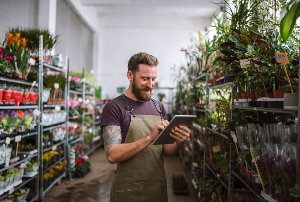 male worker in florist shop using digital tablet - detailhandel fotos stockfoto's en -beelden