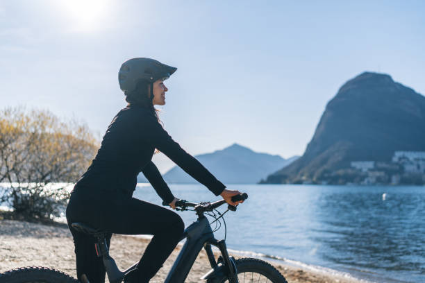 ビジネスウーマンは、湖岸に電子バイクに乗ります - ticino canton mountain lake lugano lake ストックフォトと画像