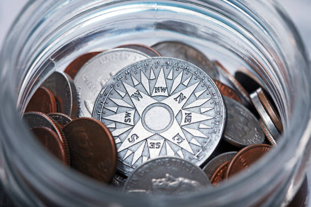 A compass rose rests among a collection of coins in a coin jar.