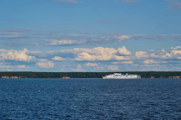 river landscape with a white ship against the background of the shore with forest and blue sky with white cloudy