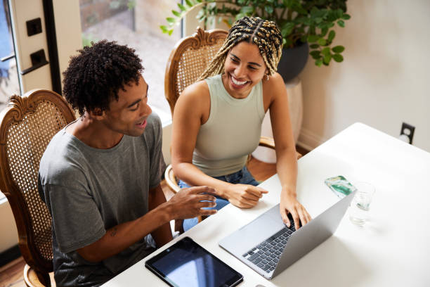 Laughing young couple using a laptop at a table at home