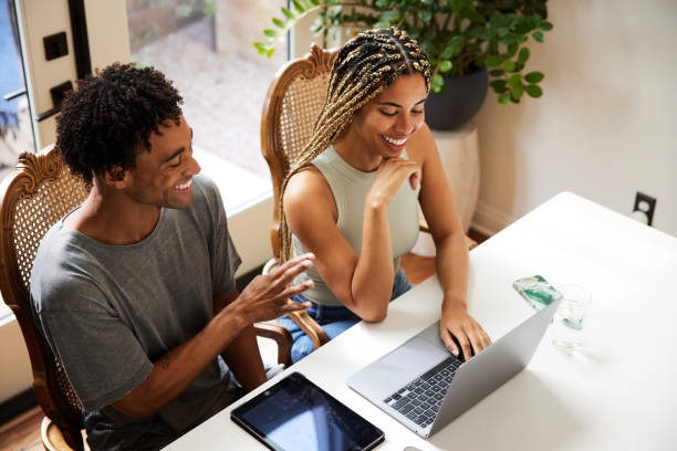istock Young couple laughing while working on a laptop together at home 1359539799