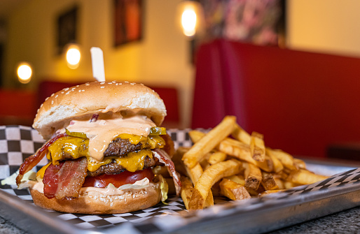 A cheesy hamburger with bacon and fries in a restaurant.