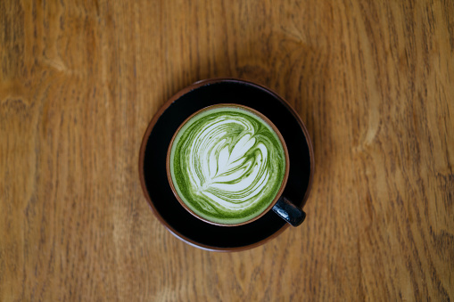 Japanese matcha green tea latte with froth art on top of wooden table
