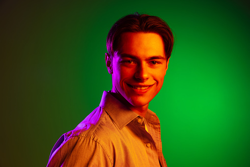Beautiful smile. Close-up face of young smiling man isolated on green studio background in neon, monochrome. Looks happy. Concept of human emotions, facial expression, sales, ad, fashion